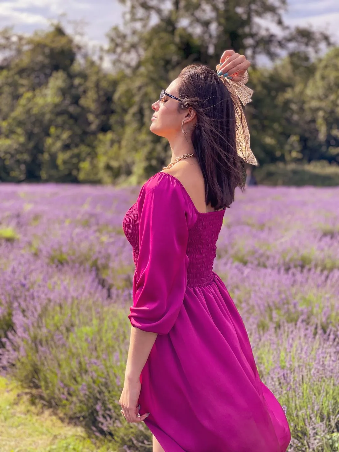 Mujer de perfil con un vestido rosa fucsia de manga larga, en un campo de lavanda.