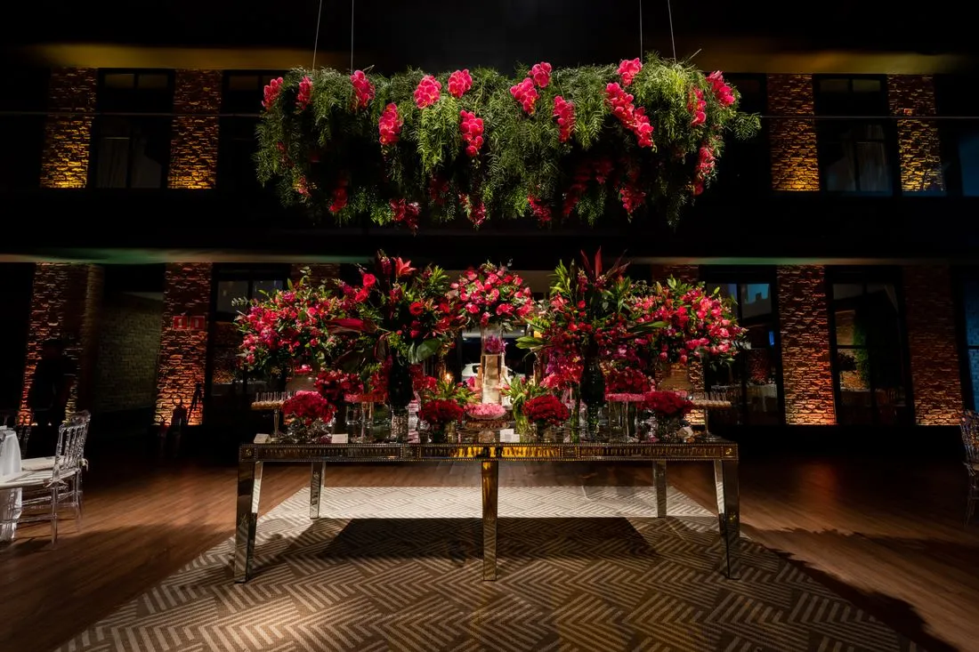 Mesa de recepción bajo un arreglo grande de flores rojas, de noche.