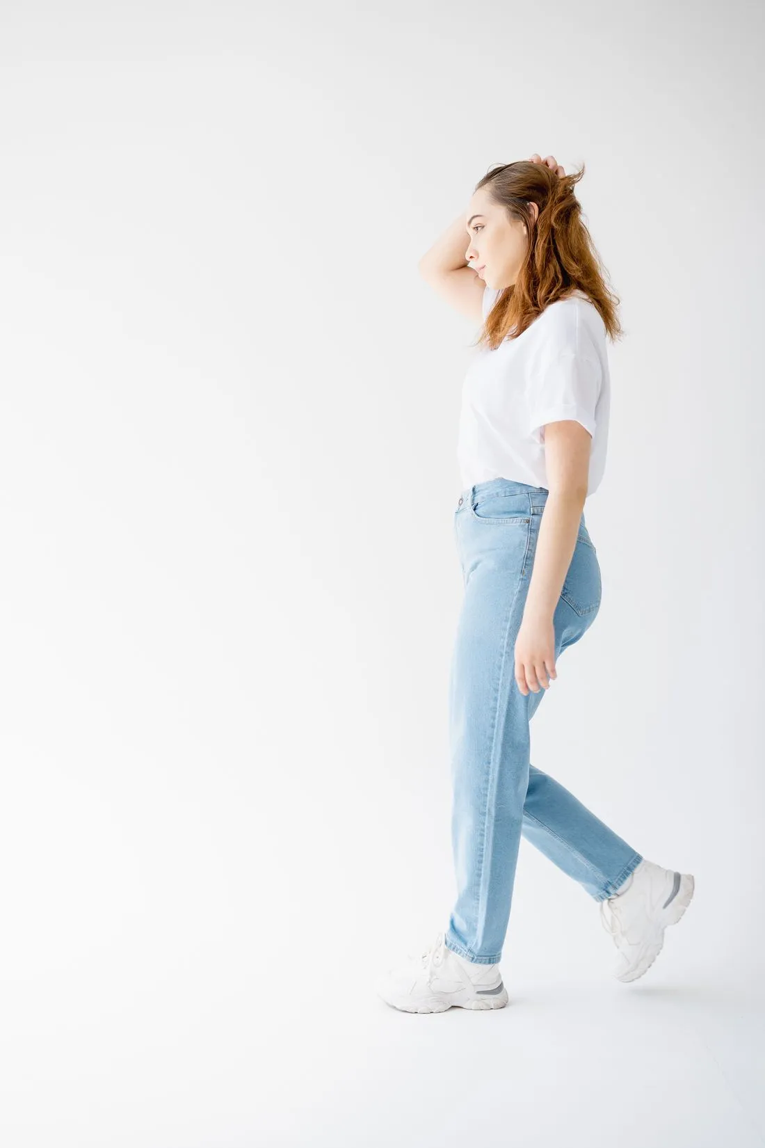 Mujer de perfil caminando, con jeans claros de tiro alto, camiseta blanca y tenis.