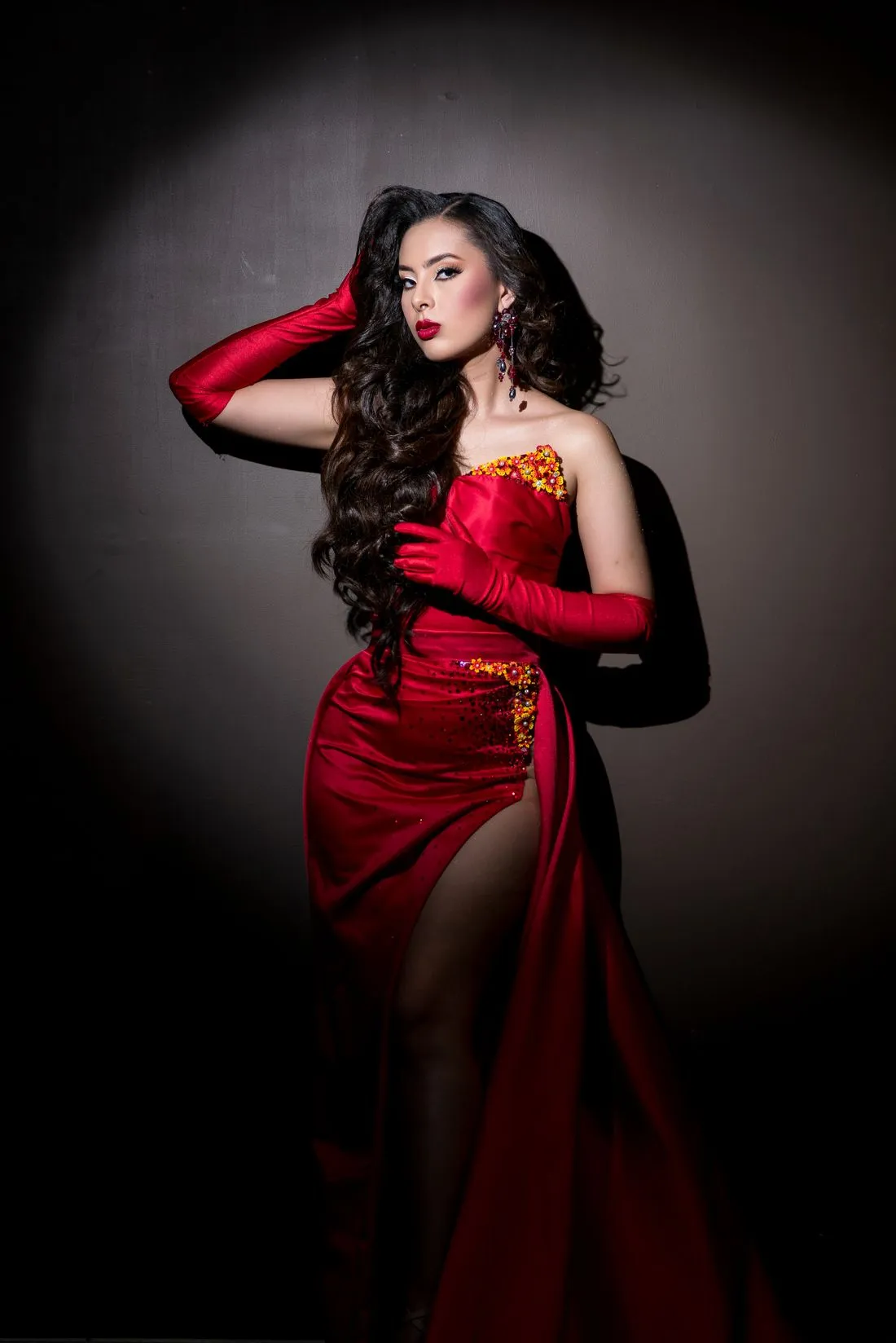 Mujer con un vestido largo rojo con abertura y guantes rojos largos, sobre fondo oscuro.