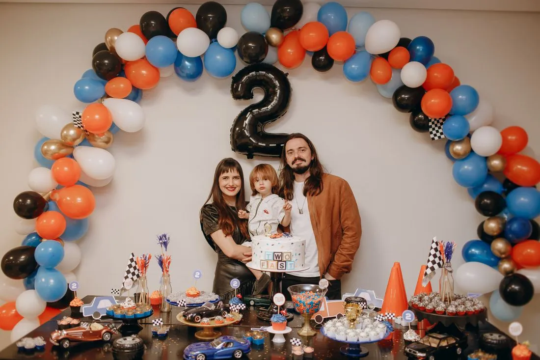 Familia frente a un arco de globos con el número 2 y una mesa de dulces.