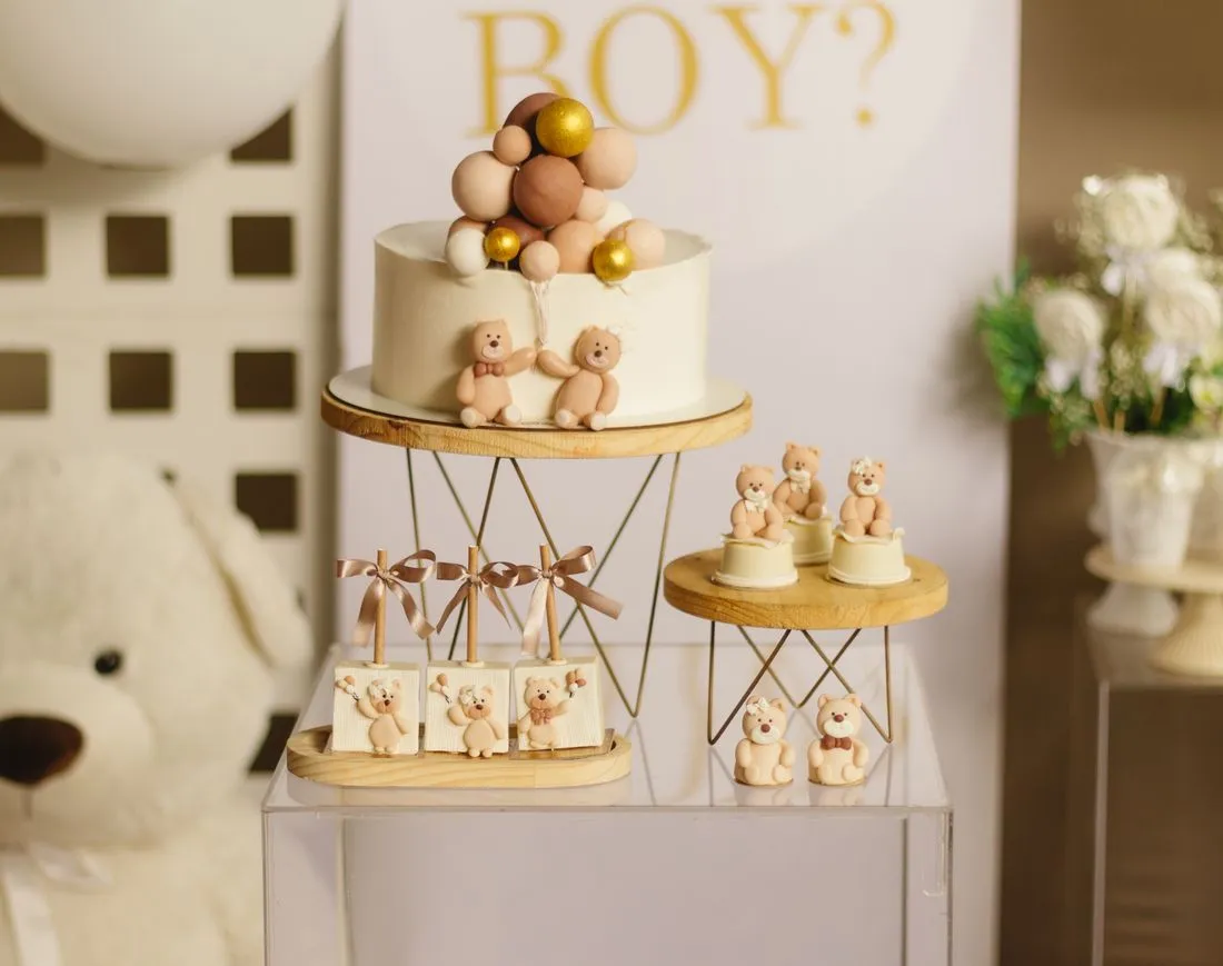Mesa de baby shower con una torta de osos de peluche y adornos dorados.