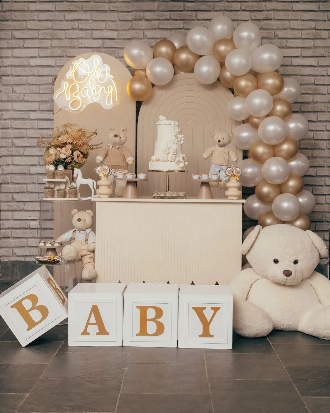 Arco de globos color crema y dorado con cubos que dicen BABY y osos de peluche.