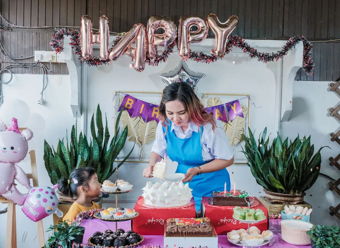 Mujer sirviendo en una mesa de dulces bajo un letrero de globos que dice HAPPY.