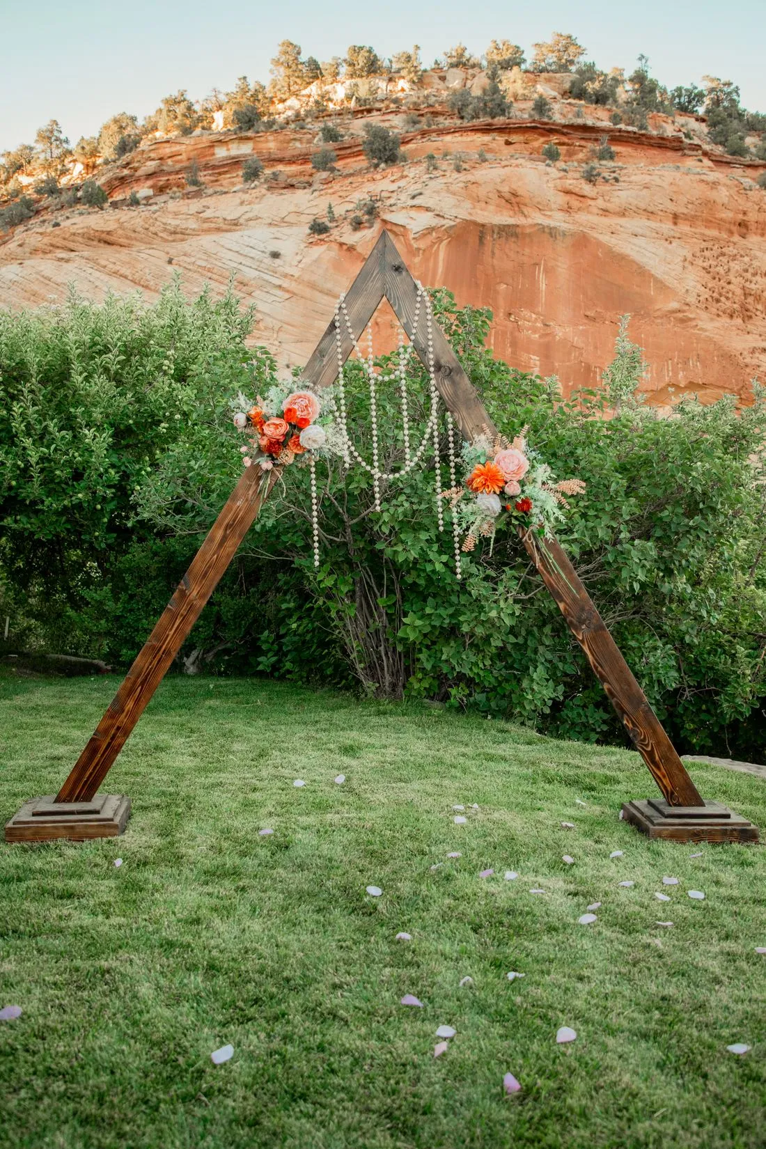 Arco triangular de madera con flores naranja sobre un jardín verde.