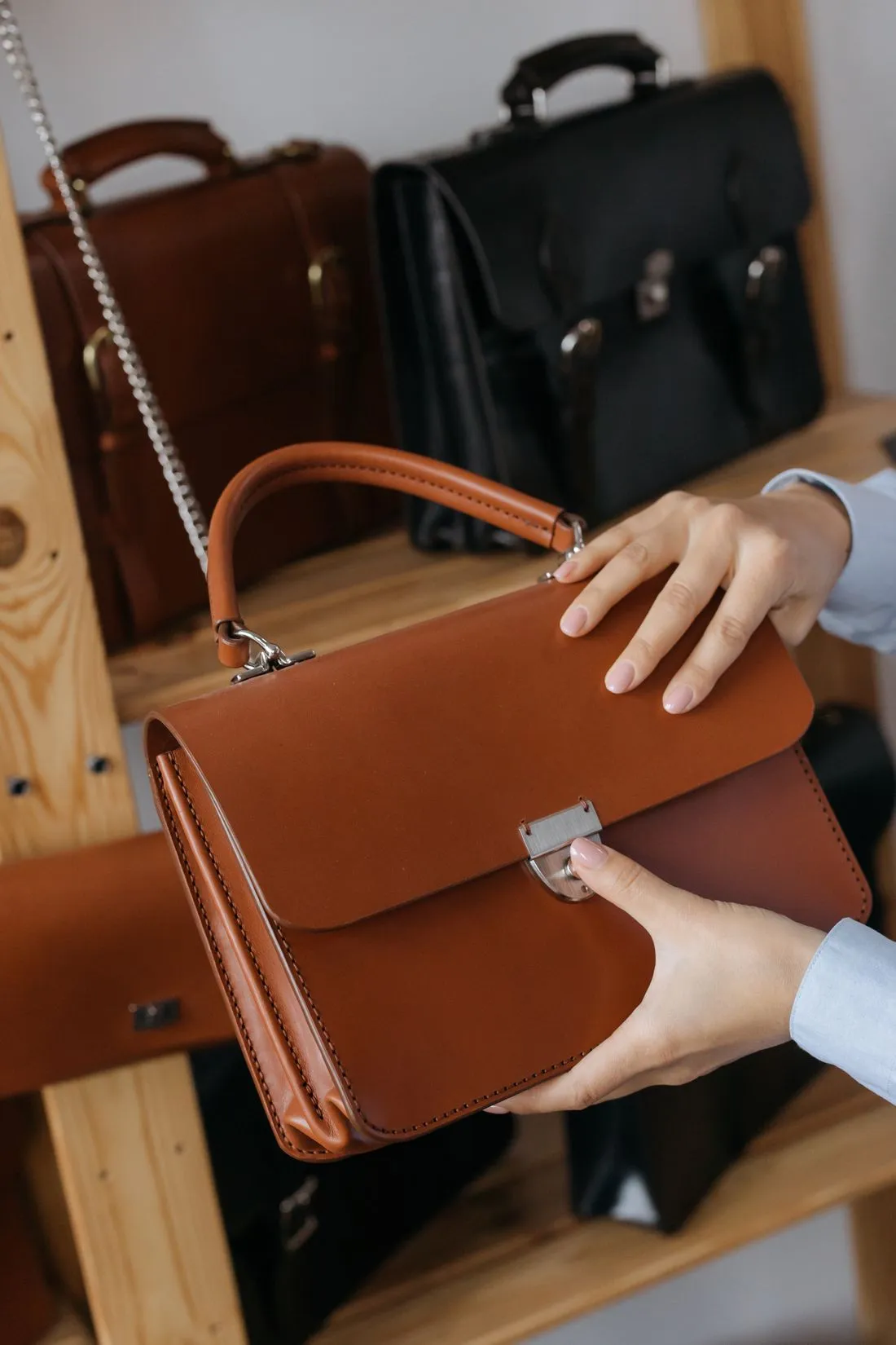 Manos sosteniendo una cartera de cuero café con cierre metálico, junto a otros bolsos.